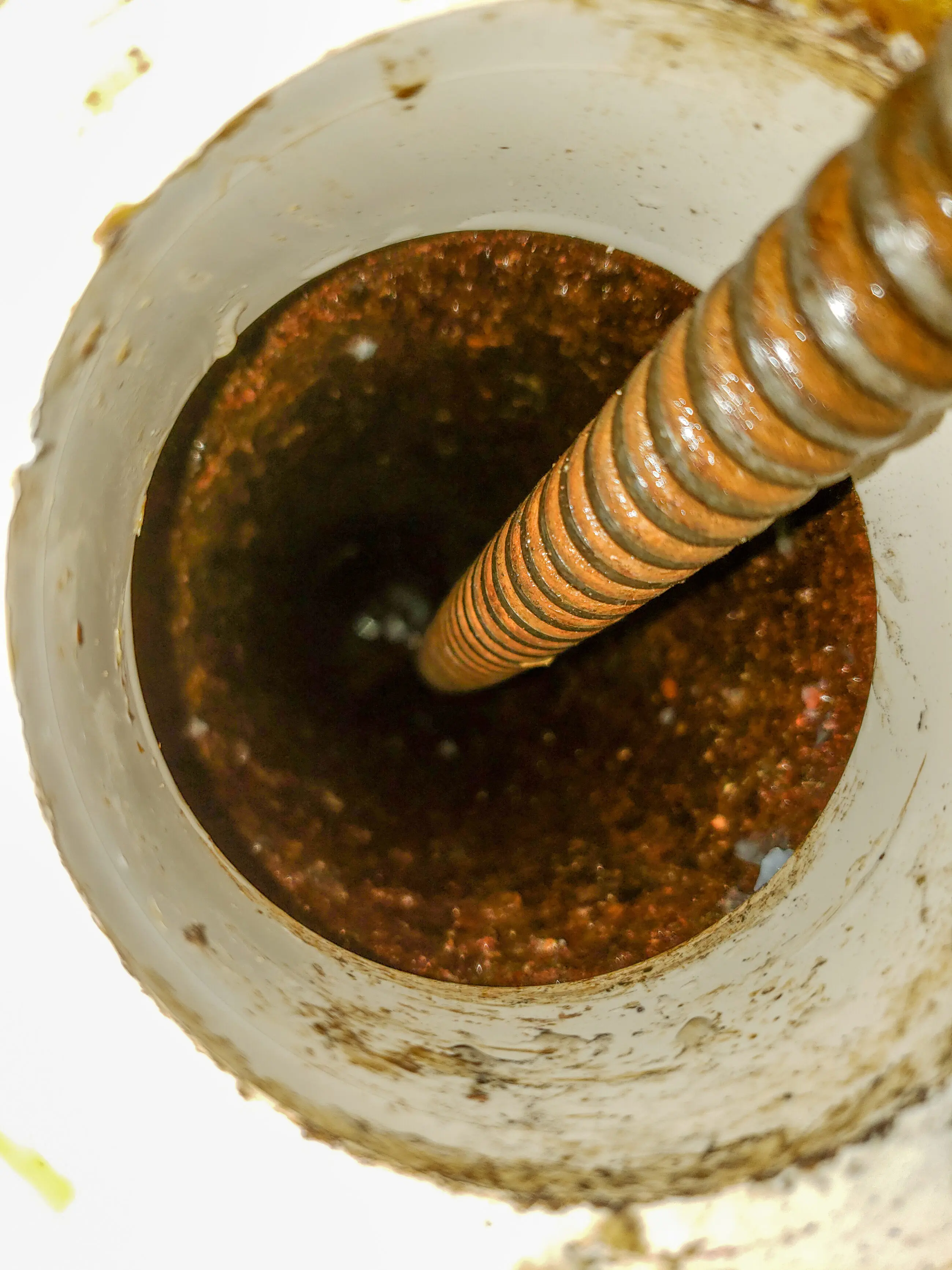 Drain Cleaning Close-up of a rusted drain pipe interior with a coiled plumbing snake inserted to clear a clog, showing corroded sediment and PVC pipe walls—plumbing drain cleaning service for homes in Bedford, Lynchburg, and Roanoke