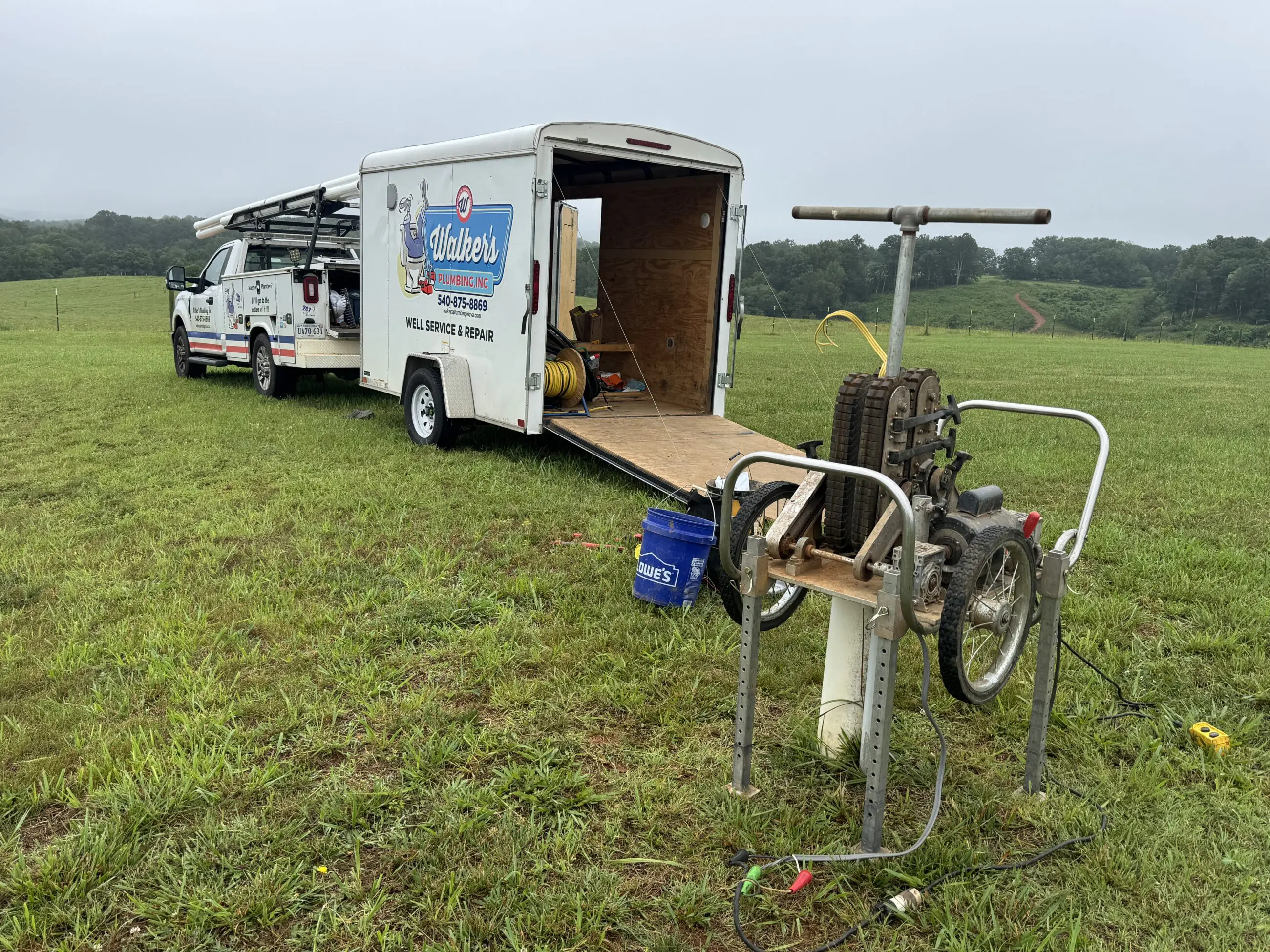 Repair or Replace Walker’s Plumbing service truck and open trailer parked on a grassy rural lot next to well-pulling equipment and hoses, showing technicians on site for well pump repair and replacement.