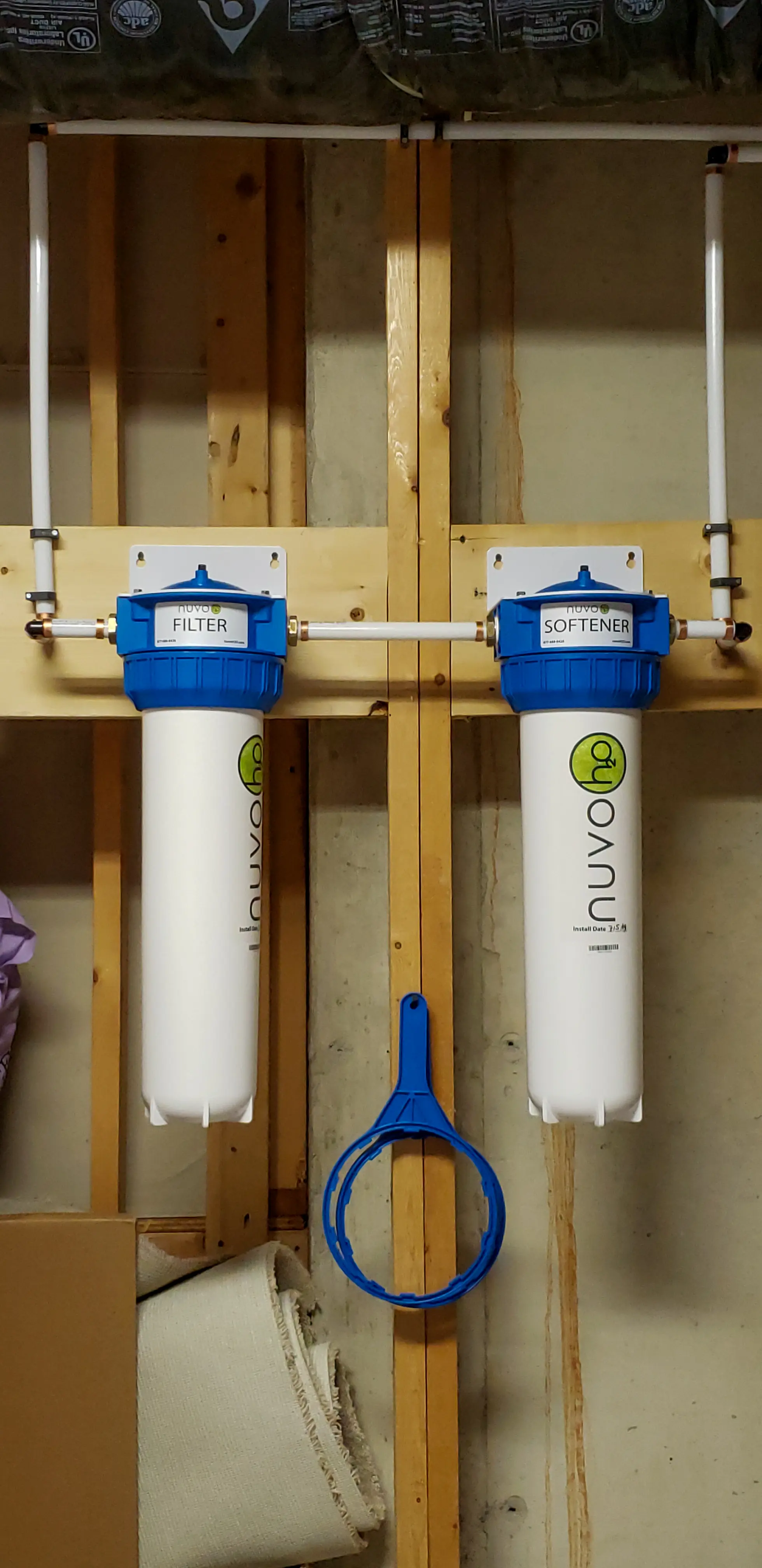 Black polyethylene water service pipe partially exposed in wet brown clay soil, close-up view showing scratches and a small leak where muddy water seeps from the buried plumbing line.